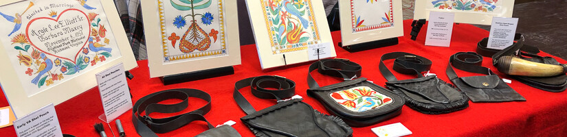 Show display table with fraktur, hunting pouches, and powder horns.